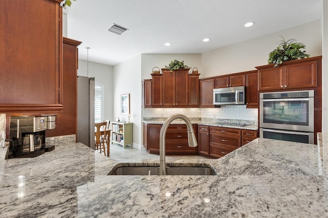 kitchen with visible vents, a sink, tasteful backsplash, stainless steel appliances, and light stone countertops
