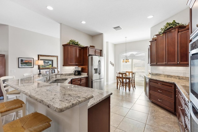 kitchen with visible vents, a breakfast bar area, a peninsula, stainless steel refrigerator with ice dispenser, and a sink
