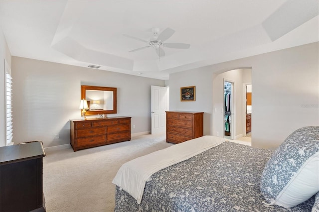 bedroom with light carpet, arched walkways, a raised ceiling, and baseboards