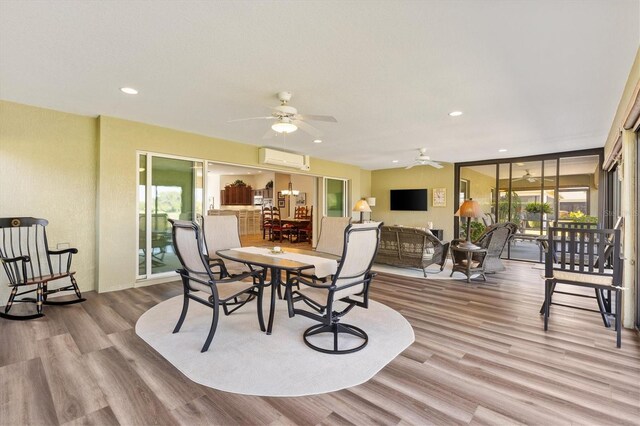 dining area featuring a wall unit AC, wood finished floors, a healthy amount of sunlight, and ceiling fan