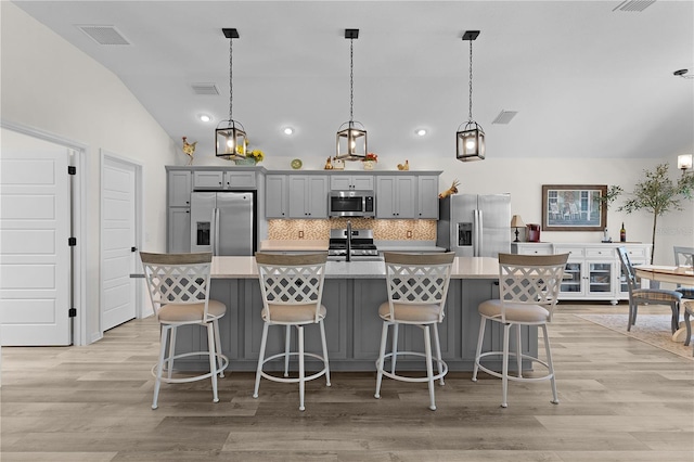 6444 Mcknight Loop, The Villages, FL 34762 - kitchen featuring stainless steel appliances, lofted ceiling, gray cabinetry, a kitchen island with sink, and decorative backsplash
