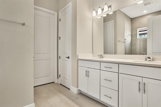 full bathroom with a tile shower, visible vents, double vanity, and a sink