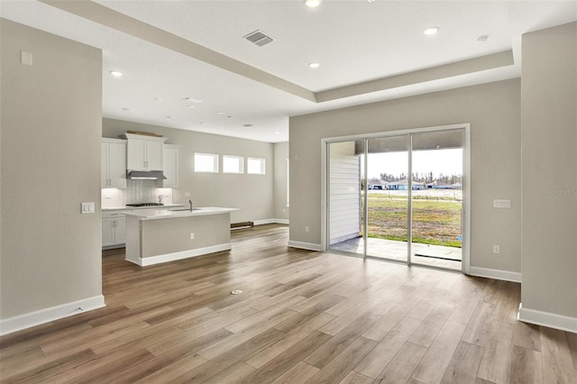 unfurnished living room with visible vents, a sink, recessed lighting, light wood-style floors, and baseboards
