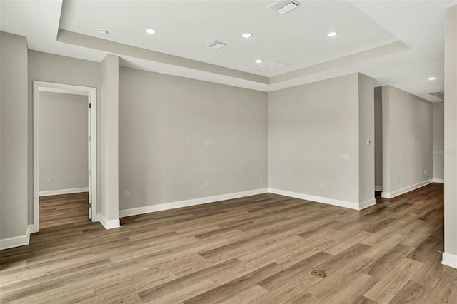 spare room featuring a raised ceiling, recessed lighting, visible vents, and light wood-type flooring