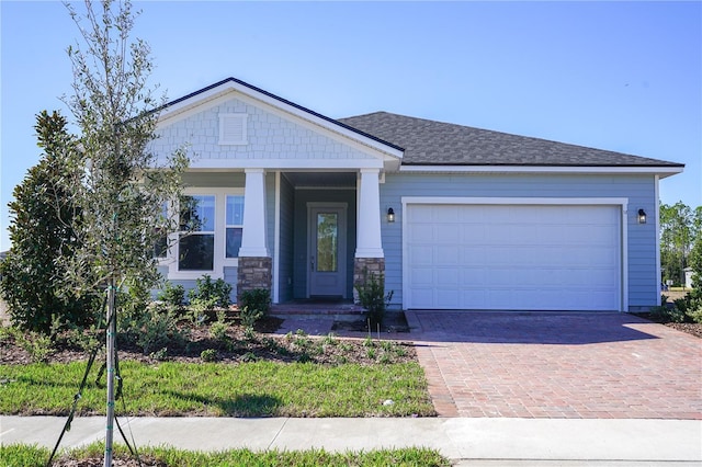 craftsman inspired home featuring decorative driveway, stone siding, and an attached garage
