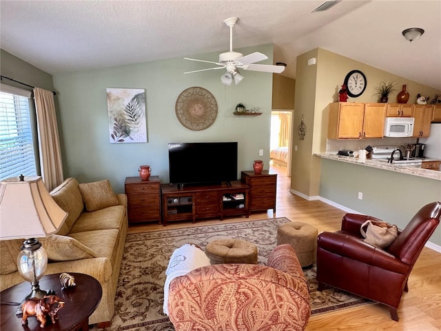 living area featuring visible vents, a ceiling fan, light wood-style floors, and vaulted ceiling