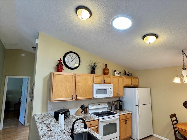 kitchen with a notable chandelier, a sink, light stone counters, white appliances, and vaulted ceiling