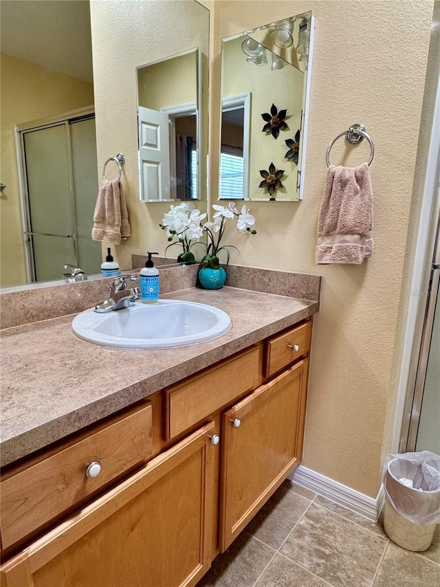 full bath with tile patterned flooring, an enclosed shower, vanity, and baseboards