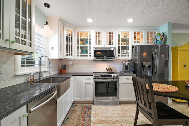 kitchen with a sink, decorative backsplash, stainless steel appliances, glass insert cabinets, and decorative light fixtures