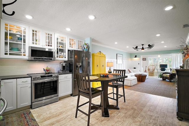 kitchen featuring dark countertops, light wood finished floors, tasteful backsplash, ornamental molding, and appliances with stainless steel finishes