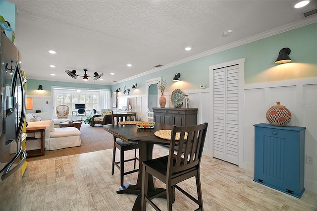 dining room featuring light wood-type flooring, visible vents, a wainscoted wall, ornamental molding, and a textured ceiling