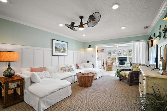 carpeted living room with a ceiling fan, a wainscoted wall, visible vents, a textured ceiling, and crown molding