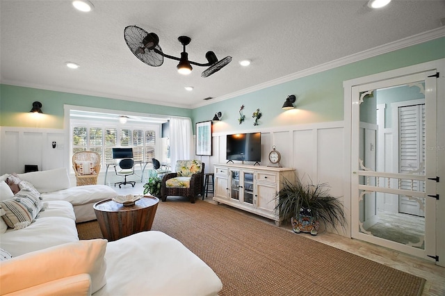 living room with a textured ceiling, ornamental molding, a ceiling fan, and a decorative wall