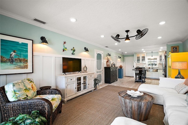 living area with visible vents, a wainscoted wall, ornamental molding, a textured ceiling, and a decorative wall