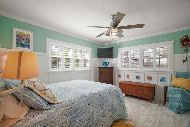 bedroom featuring a textured ceiling, a ceiling fan, wood finished floors, ornamental molding, and wainscoting