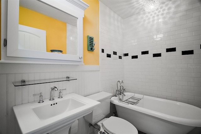 full bathroom with a sink, a freestanding bath, toilet, and wainscoting