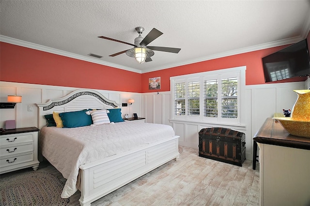 bedroom with wood finished floors, a wainscoted wall, visible vents, a textured ceiling, and crown molding