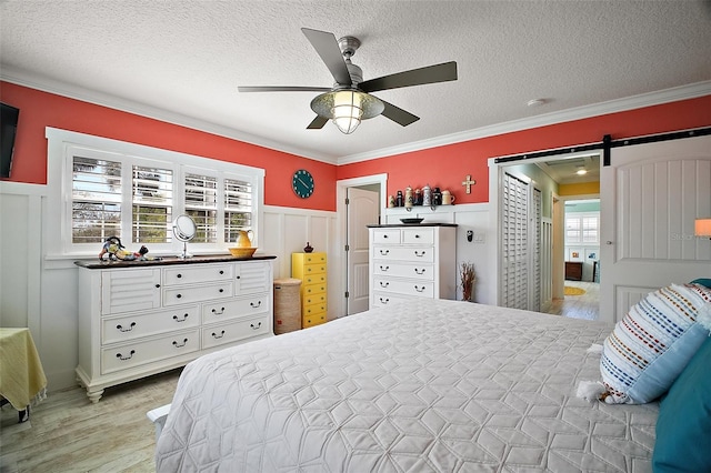 bedroom with light wood finished floors, crown molding, a wainscoted wall, a barn door, and a textured ceiling