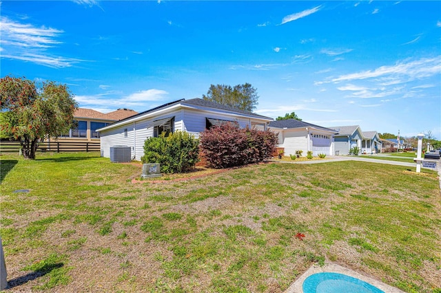 view of side of property with fence, concrete driveway, cooling unit, a yard, and an attached garage