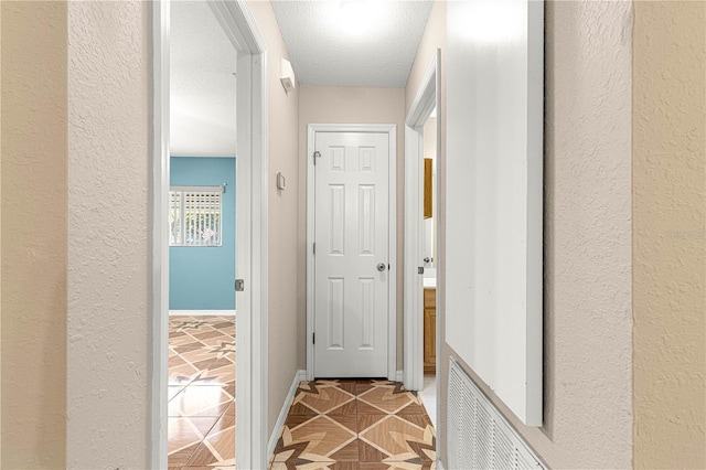 hall with tile patterned flooring, visible vents, baseboards, a textured wall, and a textured ceiling