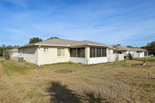 back of property featuring a sunroom, fence, central air condition unit, stucco siding, and a yard