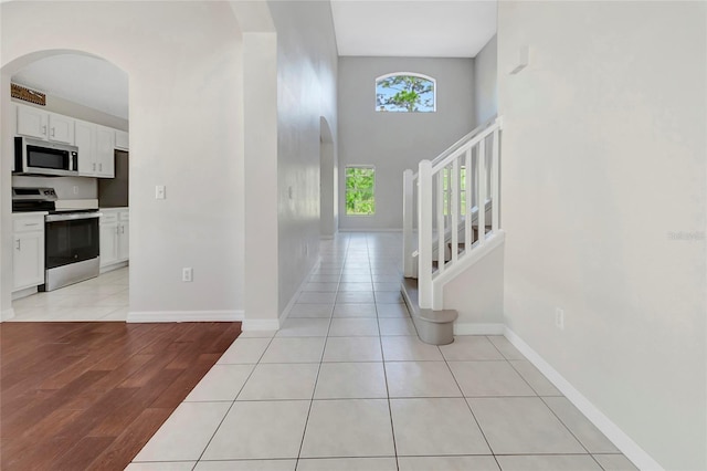 entrance foyer featuring light tile patterned floors, baseboards, a high ceiling, arched walkways, and stairs