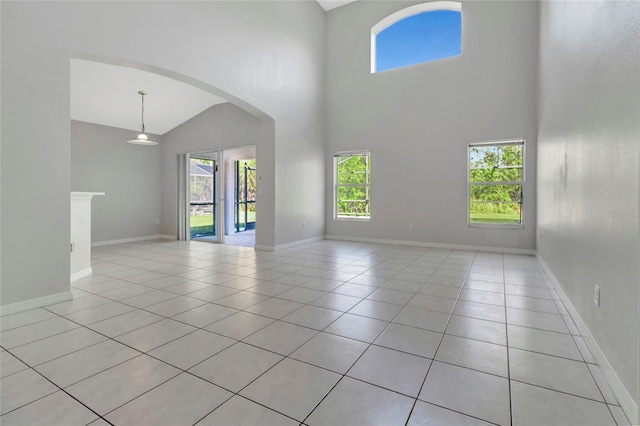 unfurnished living room with arched walkways, a high ceiling, baseboards, and light tile patterned flooring