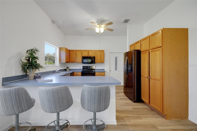2433 Tamarindo Dr, The Villages, FL 32162 - kitchen featuring a sink, a kitchen bar, a peninsula, black appliances, and light wood-style floors
