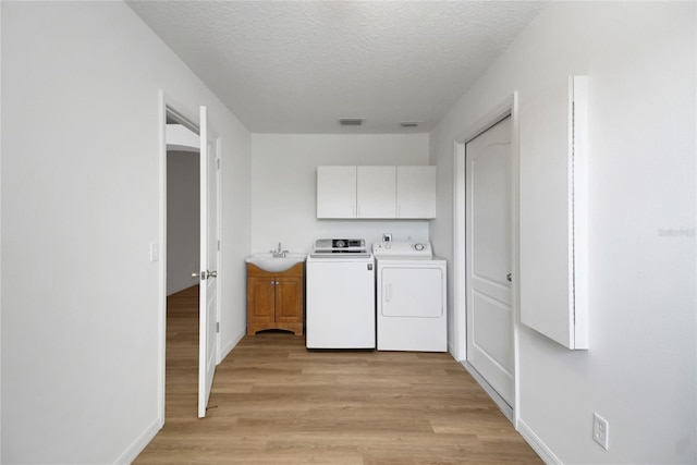 2433 Tamarindo Dr, The Villages, FL 32162 - laundry area with baseboards, a textured ceiling, light wood-style floors, cabinet space, and washing machine and dryer