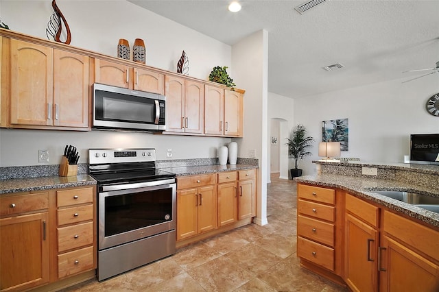 1093 Peninsula St, The Villages, FL 32162 - kitchen with stainless steel appliances, arched walkways, dark stone countertops, a ceiling fan, and a sink