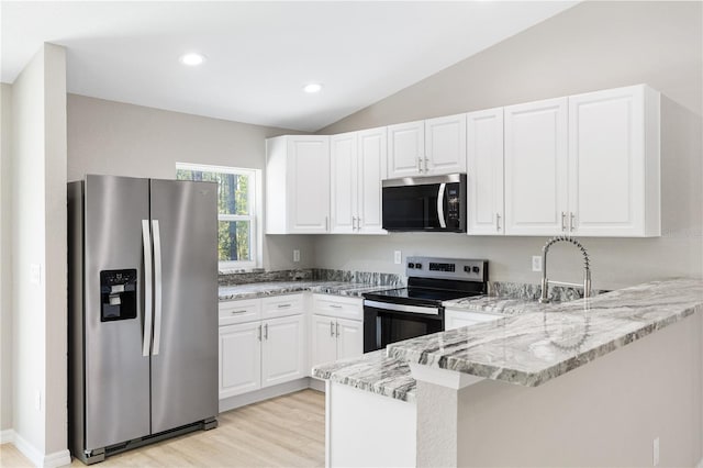 kitchen featuring vaulted ceiling, light stone counters, a peninsula, stainless steel appliances, and white cabinetry