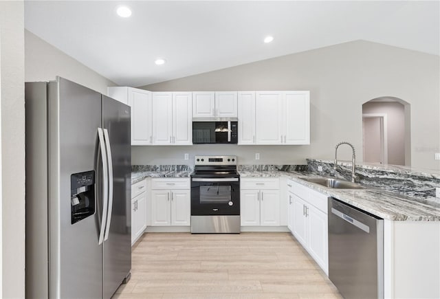 kitchen featuring light stone countertops, vaulted ceiling, arched walkways, stainless steel appliances, and a sink