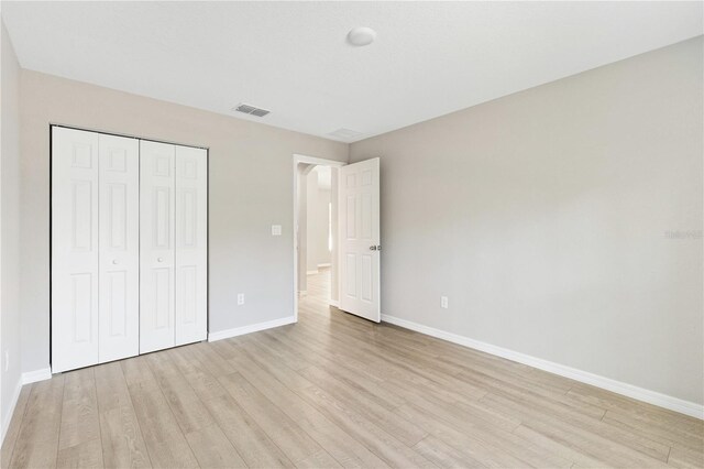 unfurnished bedroom featuring visible vents, baseboards, a closet, and light wood-style flooring