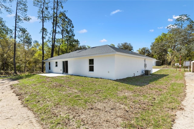 view of side of property featuring stucco siding, a lawn, and central AC