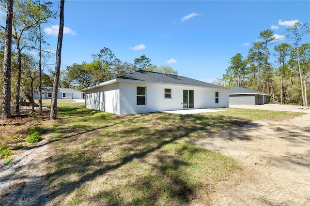 back of property featuring dirt driveway, stucco siding, a yard, a garage, and an outbuilding