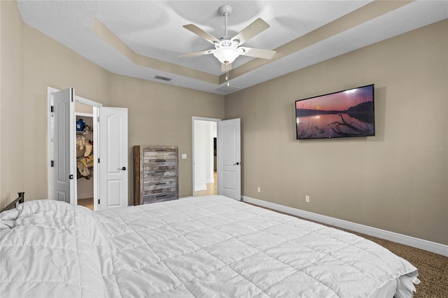 bedroom featuring a spacious closet, carpet, baseboards, a raised ceiling, and visible vents