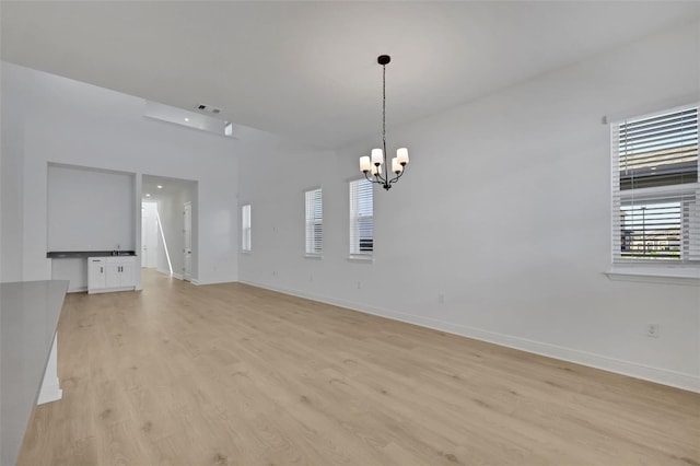 empty room featuring a notable chandelier, visible vents, a wealth of natural light, and light wood-type flooring