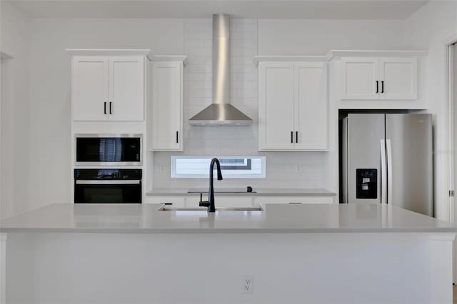 kitchen with an island with sink, light countertops, stainless steel appliances, white cabinetry, and wall chimney exhaust hood