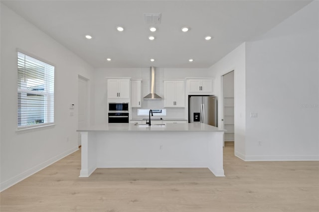 kitchen with visible vents, a center island with sink, a sink, appliances with stainless steel finishes, and wall chimney exhaust hood