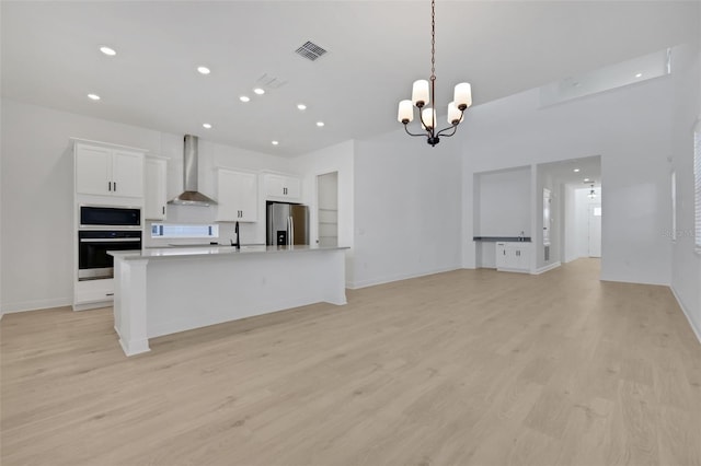 kitchen featuring oven, light wood-style flooring, wall chimney exhaust hood, stainless steel fridge with ice dispenser, and a chandelier
