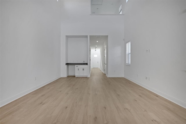 unfurnished room featuring baseboards, light wood-style flooring, and a towering ceiling