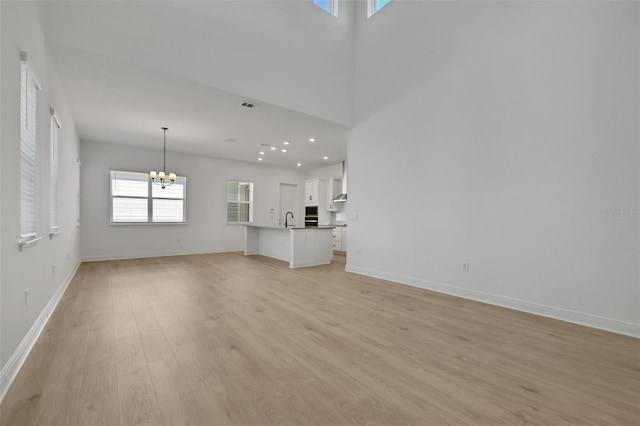 unfurnished living room featuring a sink, baseboards, light wood-style floors, and an inviting chandelier