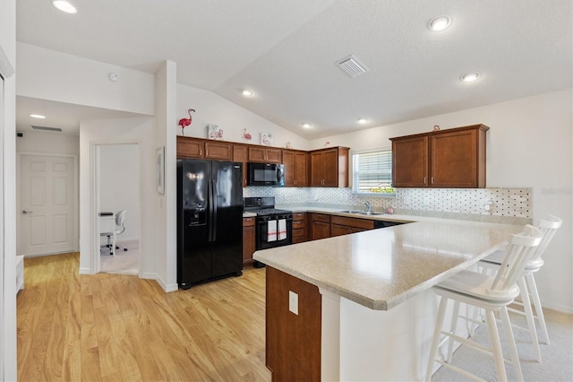 5829 Tupelo Ter, The Villages, FL 32163 - kitchen with black appliances, a peninsula, light wood-style floors, light countertops, and vaulted ceiling