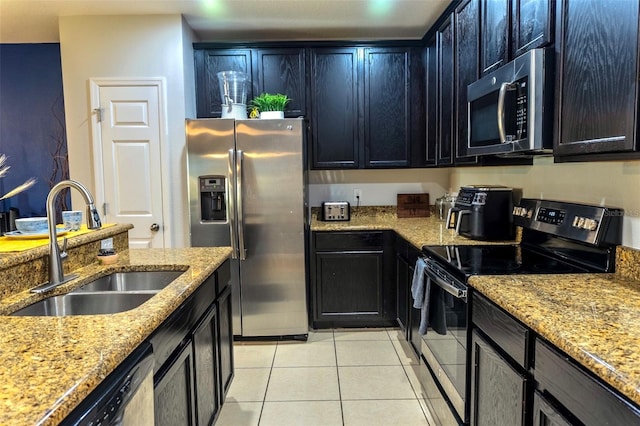 144 Primrose Dr, Davenport, FL 33837 - kitchen featuring light tile patterned floors, dark cabinetry, stainless steel appliances, a sink, and light stone countertops