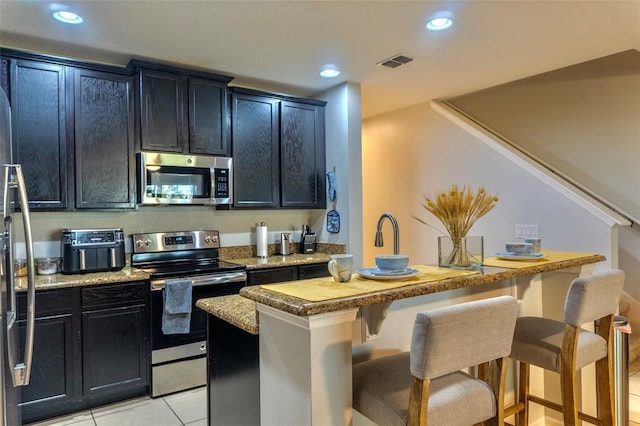 144 Primrose Dr, Davenport, FL 33837 - kitchen featuring recessed lighting, dark cabinetry, a breakfast bar, visible vents, and appliances with stainless steel finishes