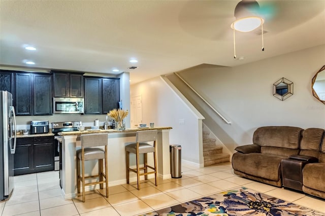 144 Primrose Dr, Davenport, FL 33837 - kitchen featuring light tile patterned floors, appliances with stainless steel finishes, dark cabinets, and a breakfast bar