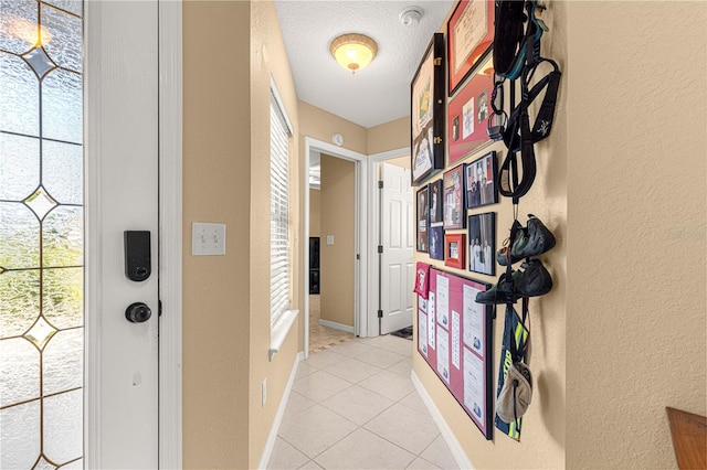hallway featuring light tile patterned flooring, a textured ceiling, baseboards, and a textured wall