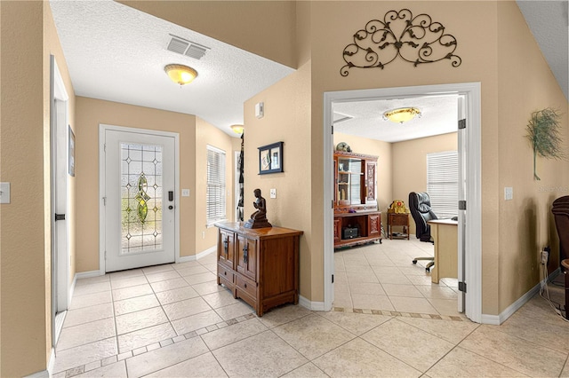 entryway with light tile patterned floors, a textured ceiling, baseboards, and visible vents
