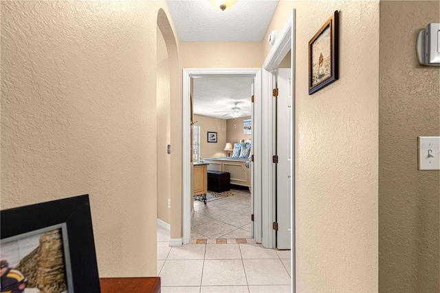 hallway with a textured ceiling, a textured wall, and light tile patterned floors