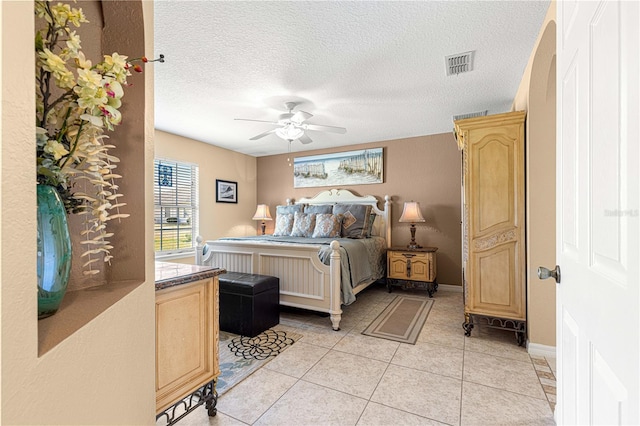 bedroom with a ceiling fan, a textured ceiling, light tile patterned floors, baseboards, and visible vents